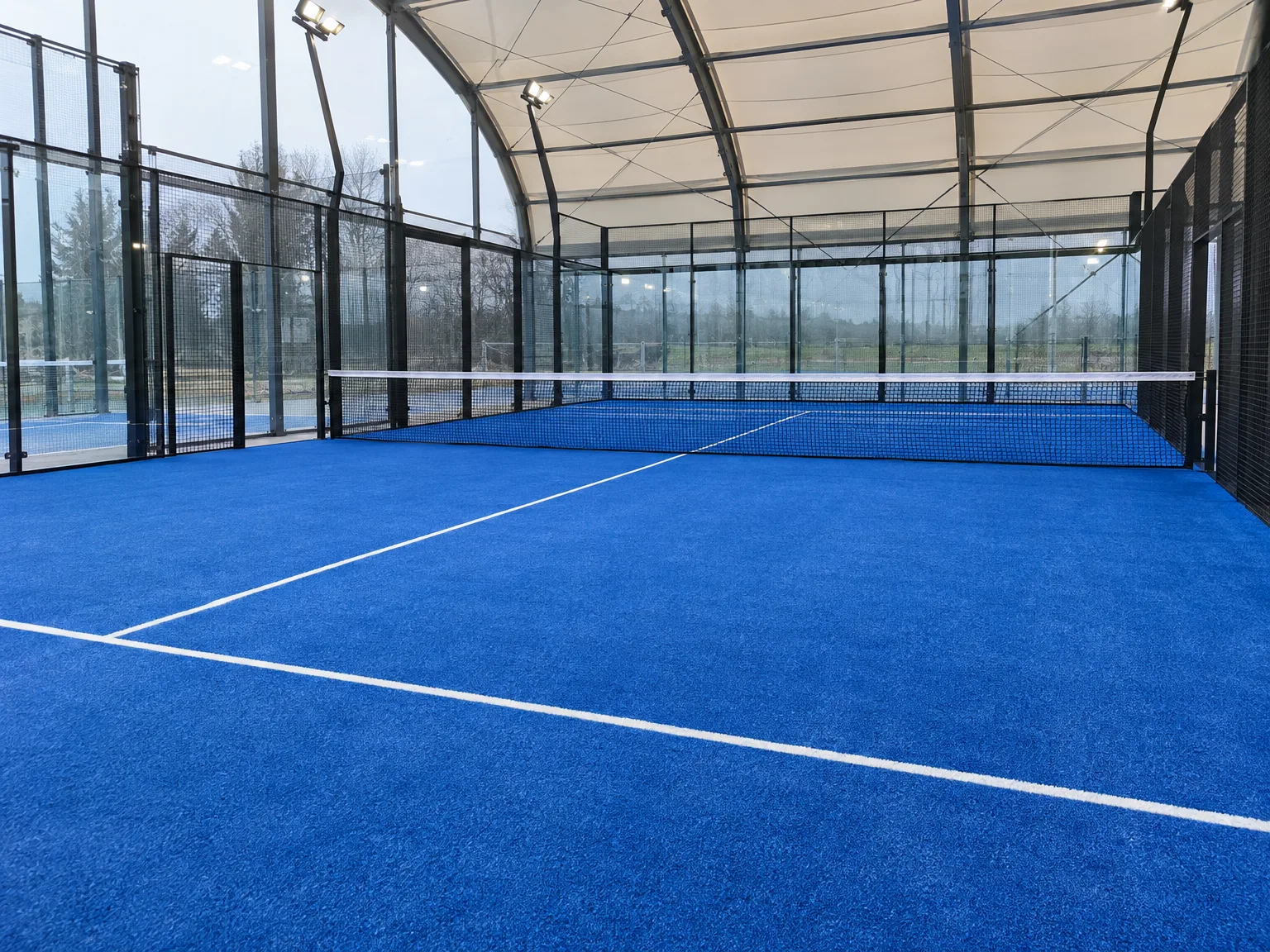 Zadasze kort do padla z niebieską nawierzchnią sportową i przeszkleniami