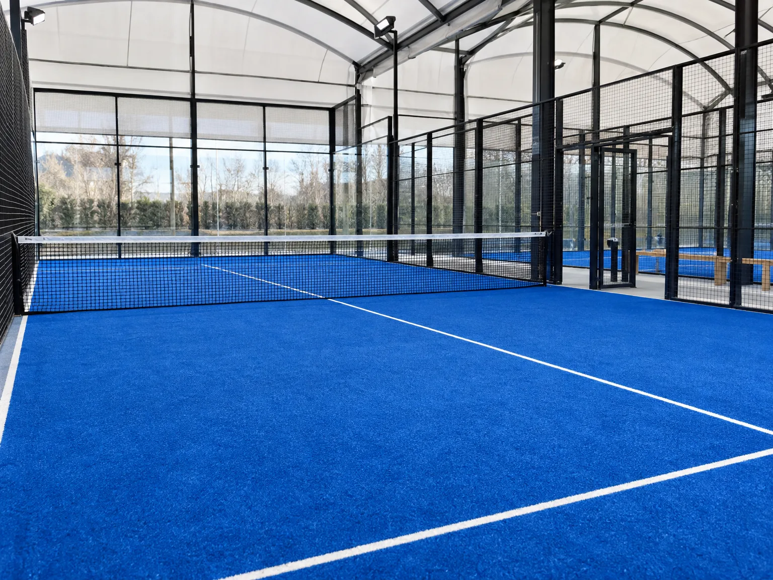 Nowoczesny kort zadaszczony do padla z niebieską nawierzchnią sportową i siatką padelową, przeszklenia hali